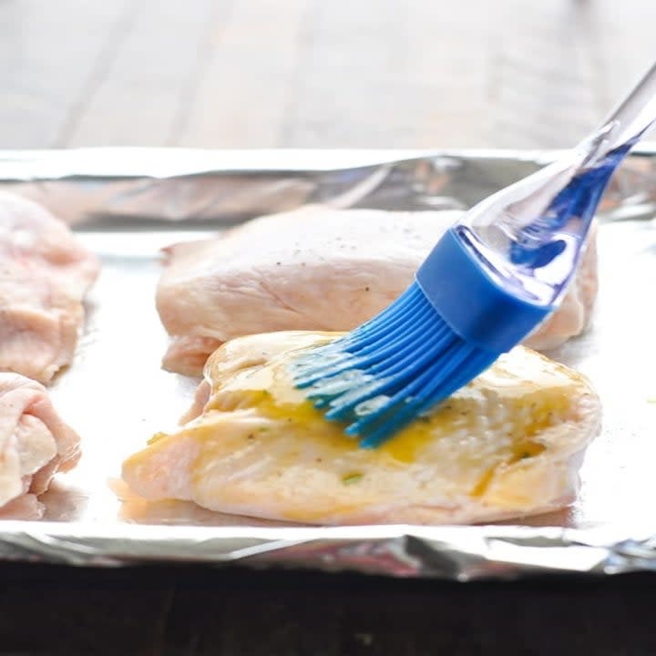 Brushing a honey mustard sauce onto skin-on chicken thighs