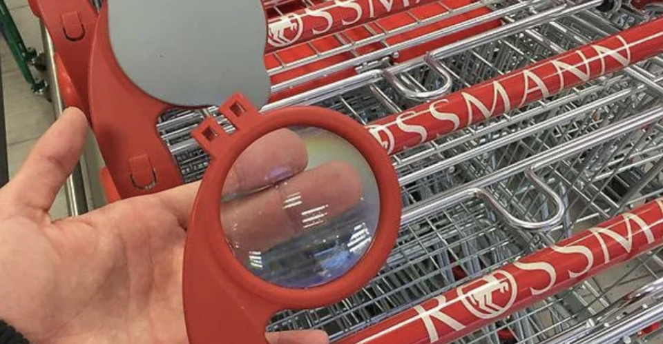 Person's fingers seen through a magnifying glass attached to a shopping cart handle