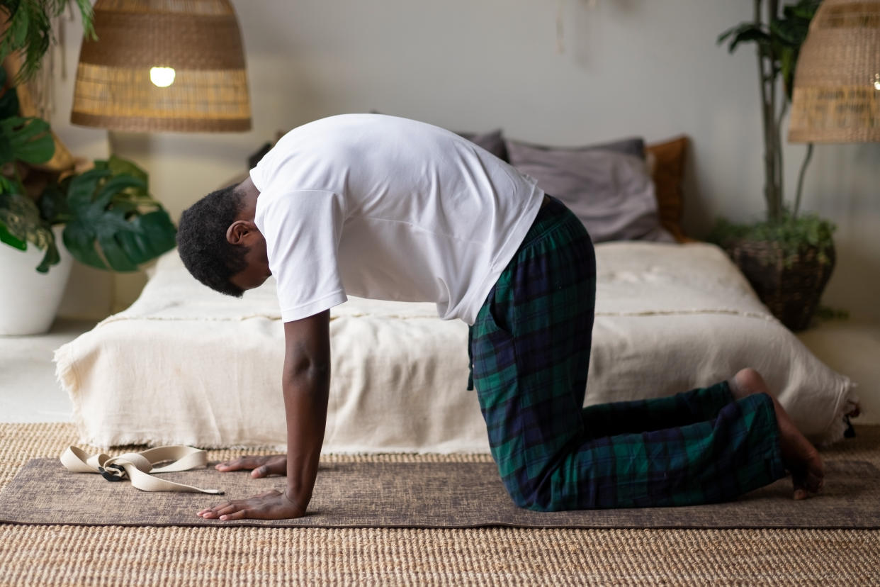 Sporty muscular young african man working out, yoga, pilates, fitness training, doing Cat Pose at home