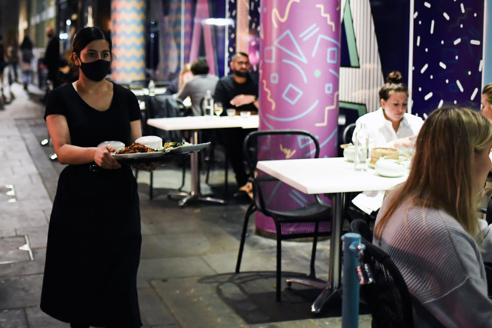 A waitress wears a protective mask as she serves customers outside a restaurant in Soho, in London, Tuesday, Sept. 22, 2020. Britain's Prime Minister, Boris Johnson, has announced that pubs and restaurants closing at 10pm, due to the spike of cases of coronavirus across the United Kingdom. (AP Photo/Alberto Pezzali)