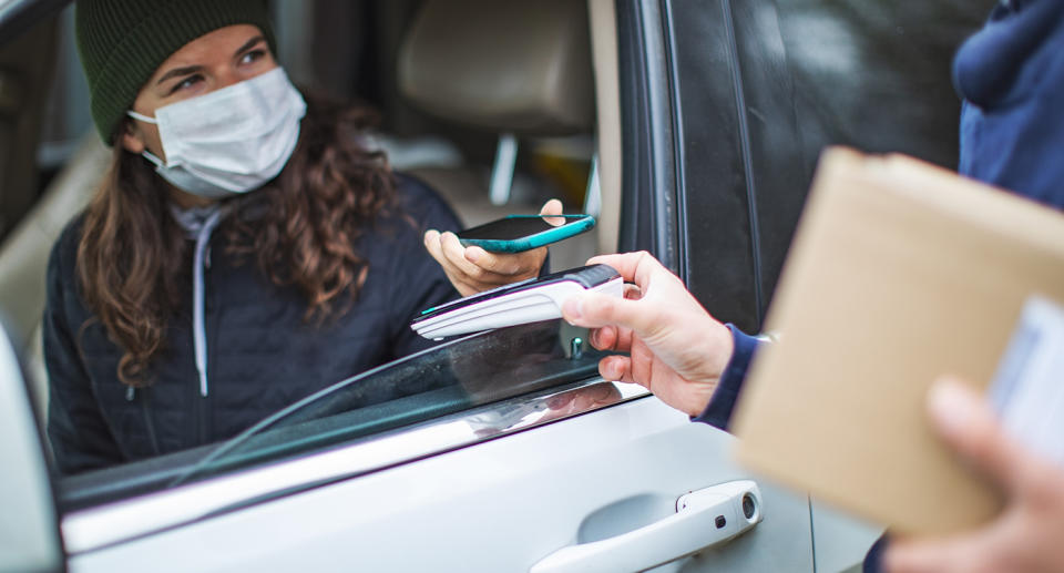 A woman pays for a food order with her phone through a car window. Source: Getty Images