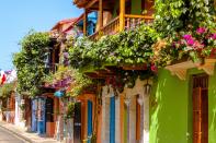 Climbing vines and bougainvillea accent the colorful façades of the homes along the streets of the walled city of Old Town in Cartagena, Colombia. The UNESCO World Heritage site is filled with colonial architecture and bustling, historic plazas.