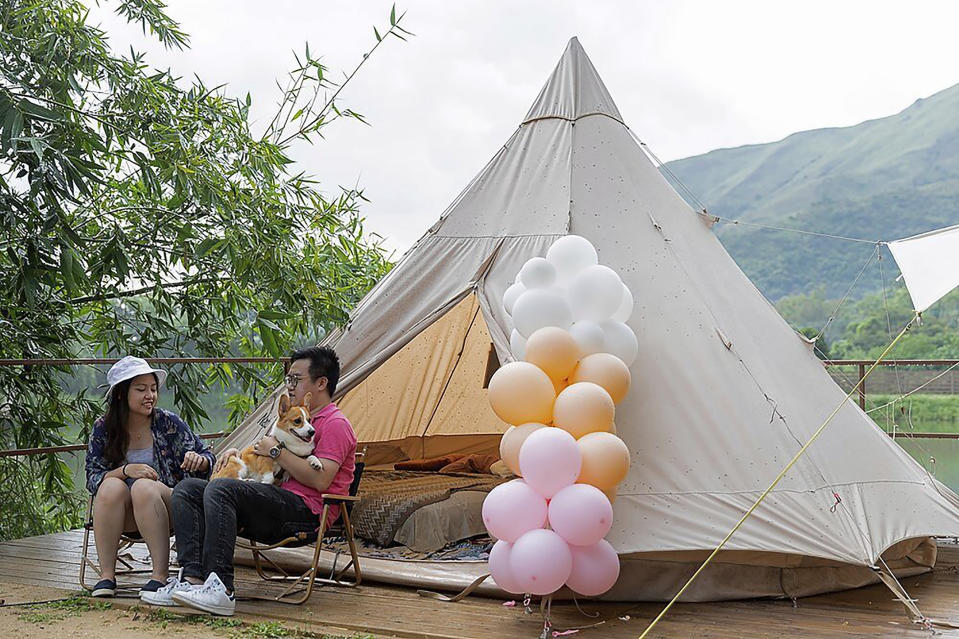 A young couple with their dog spend their time outside an Indiana-style tent at We Camp, a glamping site located in Yuen Long, Hong Kong on Aug. 19, 2021. From the Great Wall to the picturesque Kashmir valley, Asia's tourist destinations are looking to domestic visitors to get them through the COVID-19 pandemic's second year. With international travel heavily restricted, foreign tourists can't enter many countries and locals can't get out. The difficulty of traveling abroad has made glamping, or glamourous camping, popular in Hong Kong. (AP Photo/Matthew Cheng)