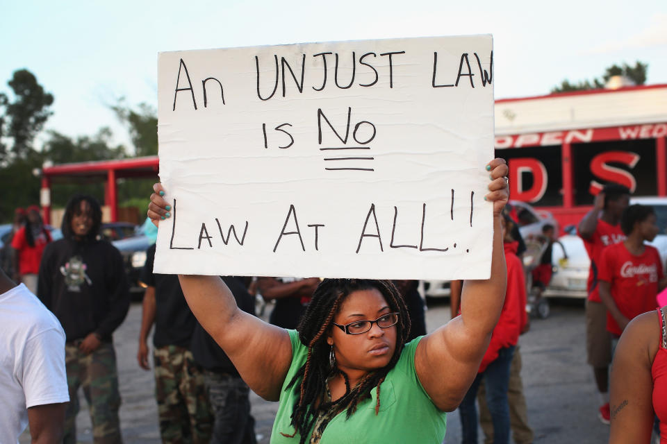 FERGUSON, MO - AUGUST 11:  Demonstrators protest the killing of 18-year-old Michael Brown who was shot by police on Saturday on August 11, 2014 in Ferguson, Missouri. Police responded with tear gas and rubber bullets as residents and their supporters protested the shooting by police of an unarmed black teenager named Michael Brown who was killed Saturday in this suburban St. Louis community. Yesterday 32 arrests were made after protests turned into rioting and looting in Ferguson.  (Photo by Scott Olson/Getty Images)