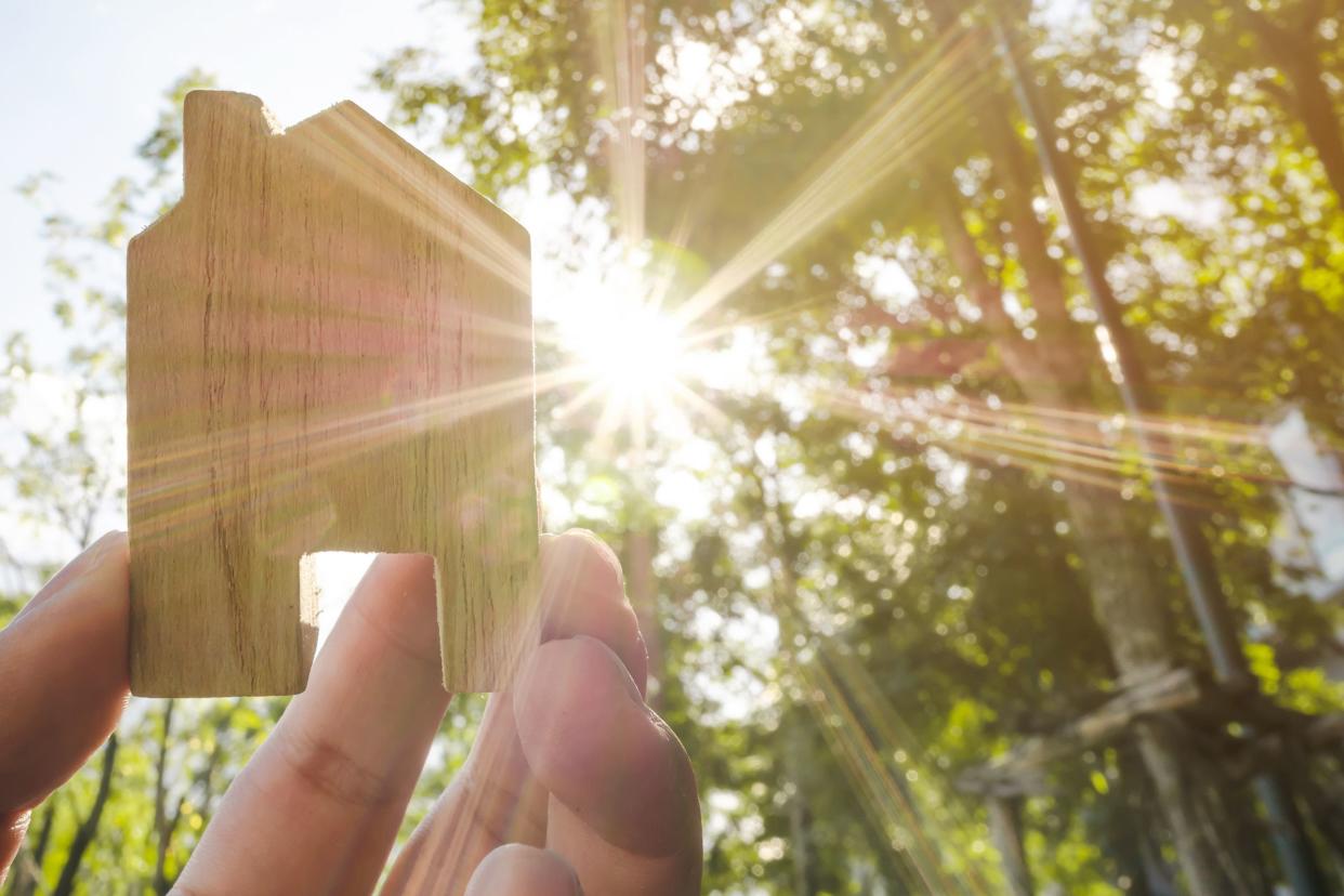 hand holding wooden house with green forest background blurred and sun lighting