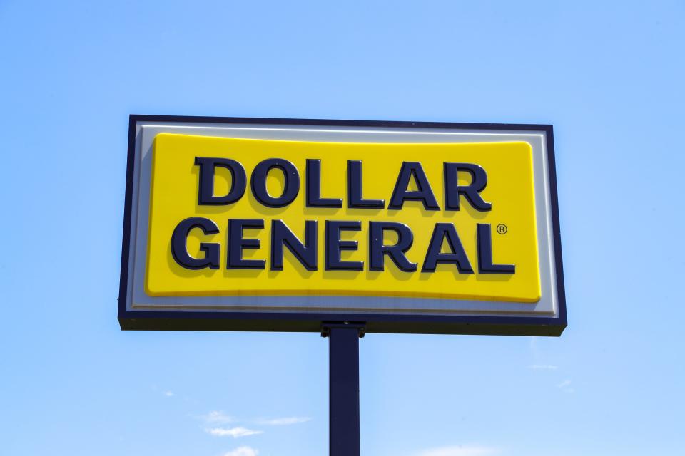 A yellow Dollar General sign with black lettering stands against a blue sky