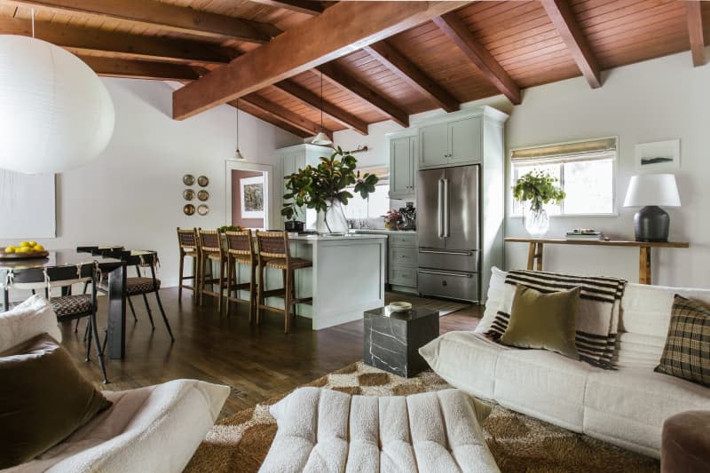 Red wood ceiling with large beams, white boucle sofas, kitchen island with cane backed bar stools, large paper mache lighting fixture