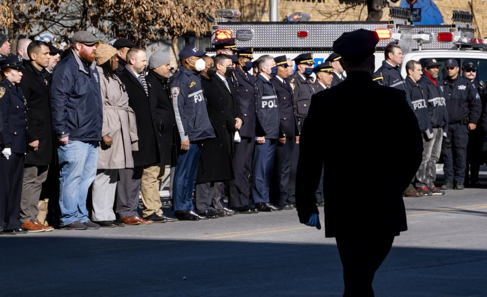 Police officers and New York City Mayor Eric Adams, center left wearing mask, stand at attention after the remains of New York City Police Department Officer Wilbert Mora arrived at a funeral home in the Manhattan borough of New York, Wednesday, Jan. 26, 2022. Officer Mora, who died Tuesday, was gravely wounded last week in a Harlem shooting that also killed his partner. (AP Photo/Craig Ruttle)