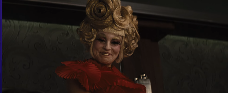 She tops it off with a metallic gold wig to match Katniss's pin, and her emotional declaration that she, Haymitch, and their two Victors are a team that can't be broken apart by the Capitol is one of the first whispers of her growing sympathy toward her two District charges.