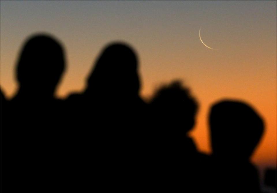 Muslims look at the crescent moon.