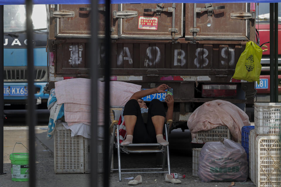 A woman browses a smartphone near a truck inside the Xinfadi wholesale food market district in Beijing, Sunday, Sept. 6, 2020. According to local news report, Xinfadi market, the capital's biggest wholesale food market have reopen for wholesale operation after it was shutdown following the coronavirus outbreak. China's government on Sunday reported several new coronavirus infections, all believed to have been acquired abroad, and no deaths. (AP Photo/Andy Wong)