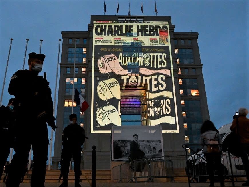 Police officers stand guard as cartoons of French satirical weekly newspaper Charlie Hebdo are projected onto the facade of the Hotel de Region in Montpellier, on 21 October, 2020 (AFP via Getty Images)