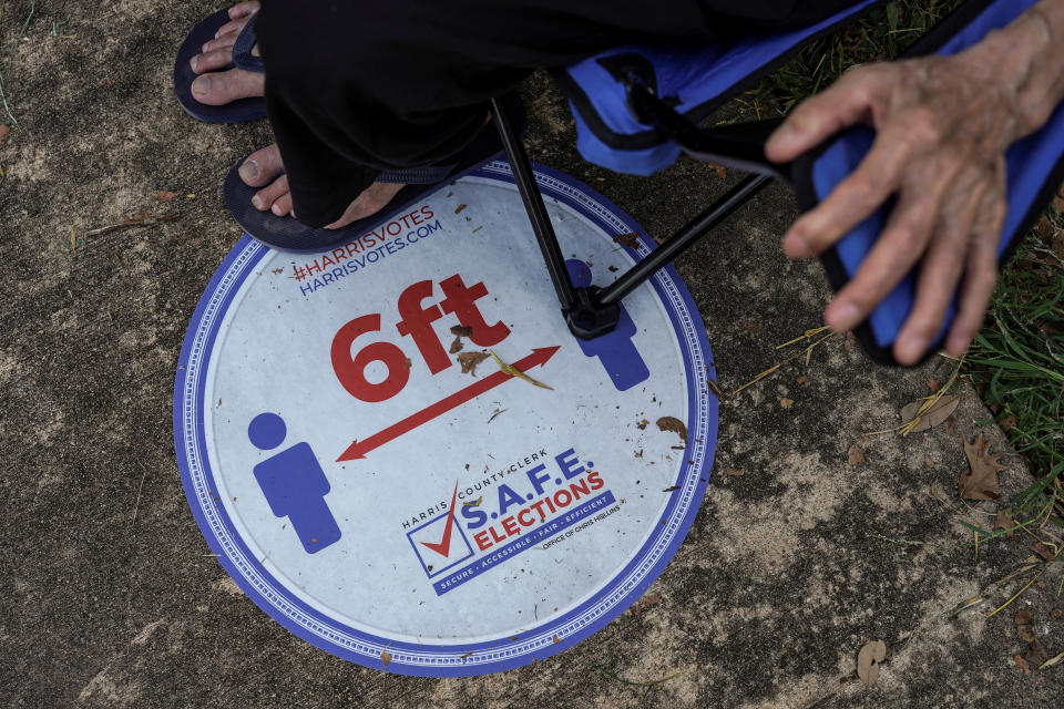 A sign to remind voters on social distancing is placed on a floor as person sits on a portable chair while waiting in line to cast his ballot for the upcoming presidential election as early voting begins in Houston, Texas, U.S., October 13, 2020.  REUTERS/Go Nakamura