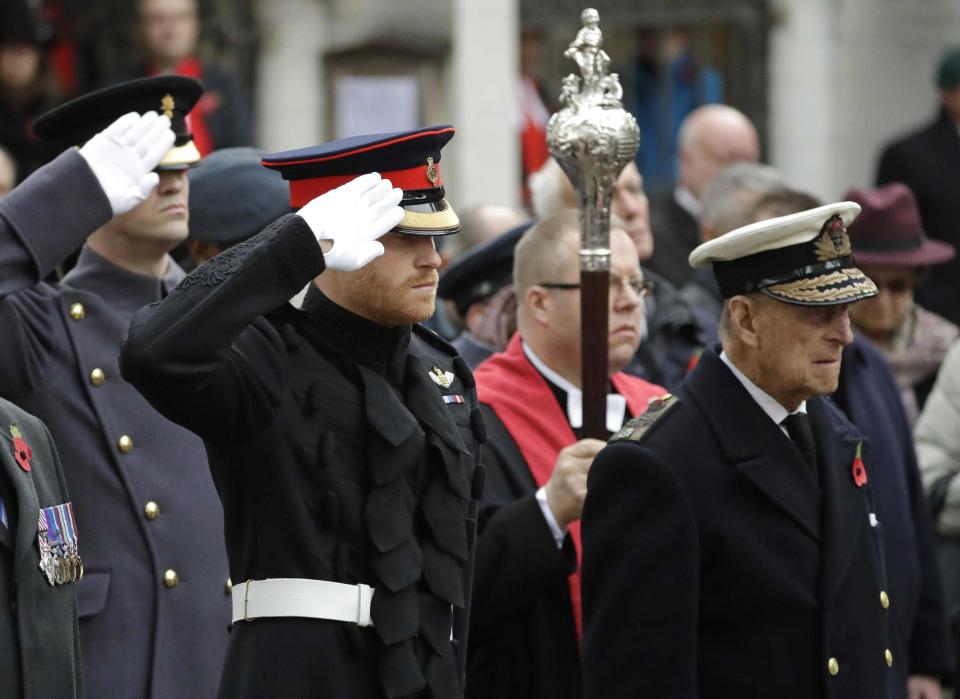 FILE - In this file photo dated Thursday, Nov. 10, 2016, Britain's Prince Harry salutes as he and Prince Philip attend the official opening of the annual Field of Remembrance at Westminster Abbey in London. The Field of Remembrance pays tribute to all the people who have served in the British armed forces since World War I. Prince Philip who died Friday April 9, 2021, aged 99, lived through a tumultuous century of war and upheavals, but he helped forge a period of stability for the British monarchy under his wife, Queen Elizabeth II. The decades brought family troubles, including the self-exile of grandson Prince Harry and his wife Meghan amid allegations of racism.(AP Photo/Matt Dunham, FILE)