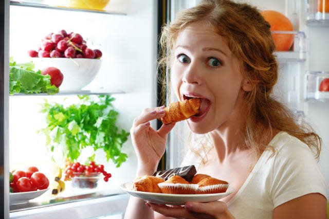 woman eats sweets at night to sneak in a refrigerator