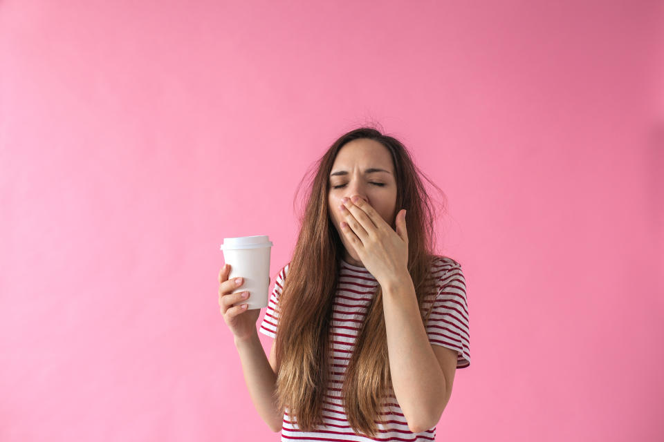 Cute girl with a glass of coffee in hand is yawning. She can't wake up.