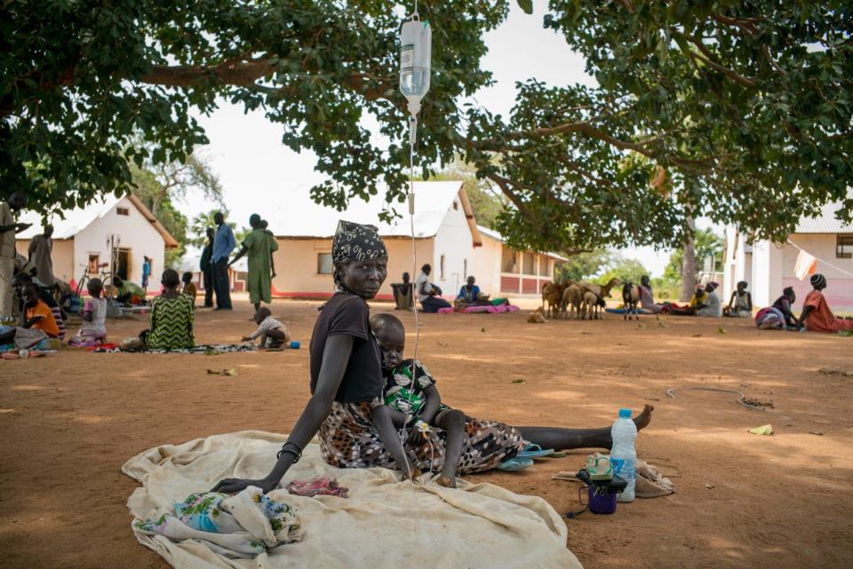 An IV drip hangs from a tree as a young girl, in her mother's arms, receives treatment.