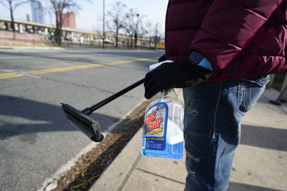 Shamonte Jones holds a bottle of window washing fluid and a squeegee as he waits for commuters to let him clean their vehicle's windshield in exchange for cash, Tuesday, Jan. 10, 2023, in Baltimore. Local officials are rolling out their latest plan to steer squeegee workers away from busy downtown intersections and toward formal employment using law enforcement action and outreach efforts. (AP Photo/Julio Cortez)