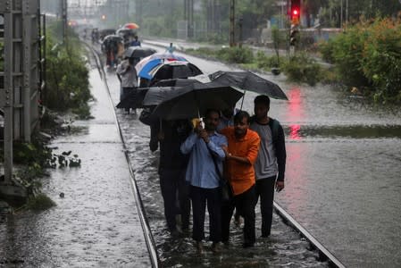Commuters walk on waterlogged railway tracks after getting off a stalled train during heavy monsoon rains in Mumbai