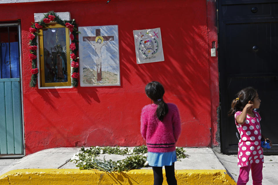 Girls look at a home where an embroidery reading "Samantha" hangs next to an image of Jesus and Or Lady of Guadalupe, during a vigil by activists from the "Women from the Periphery for the Periphery Collective" honoring 2-year-old Samantha who was found dead in June, as the group protests femicide in Ecatepec, Mexico, Sunday, Oct. 6, 2019. The collective of activists and the relatives of murdered females visited four sites where females were found dead in Ecatepec, in the state of Mexico where authorities declared in 2015 an alert concerning gender violence against women. (AP Photo/Ginnette Riquelme)