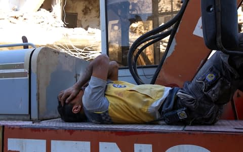 A member of the Syrian civil defence, known as the White Helmets, rests atop an excavator after participating in a search for victims under the rubble of buildings, - Credit: ABDULAZIZ KETAZ/AFP/Getty Images