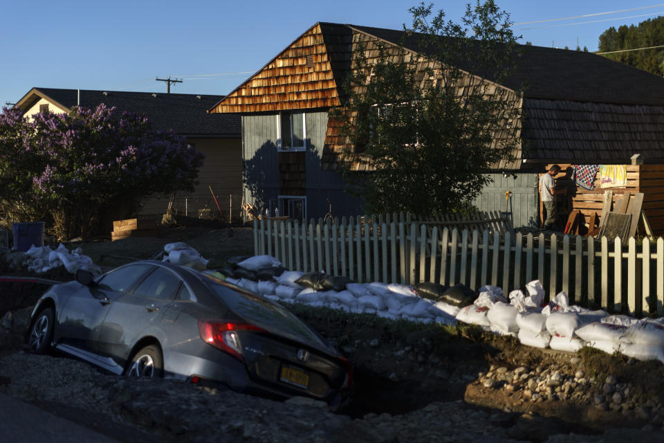 A resident fixes a fence damaged from Rock Creek floodwaters as a car rests in a washed out street in Red Lodge, Mont., Wednesday, June 15, 2022. (AP Photo/David Goldman)