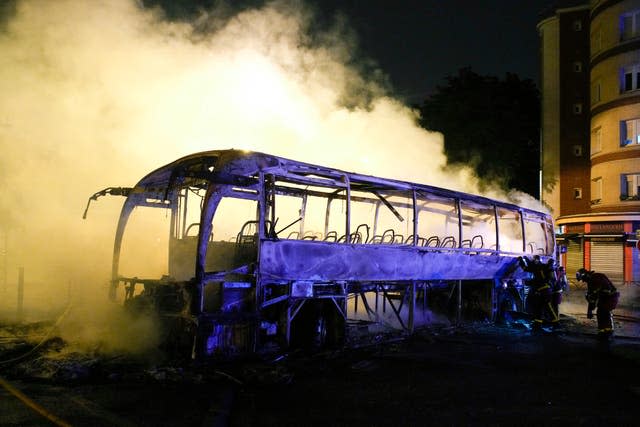 Firefighters use a water hose on a burnt bus in Nanterre, outside Paris (Lewis Joly/AP)