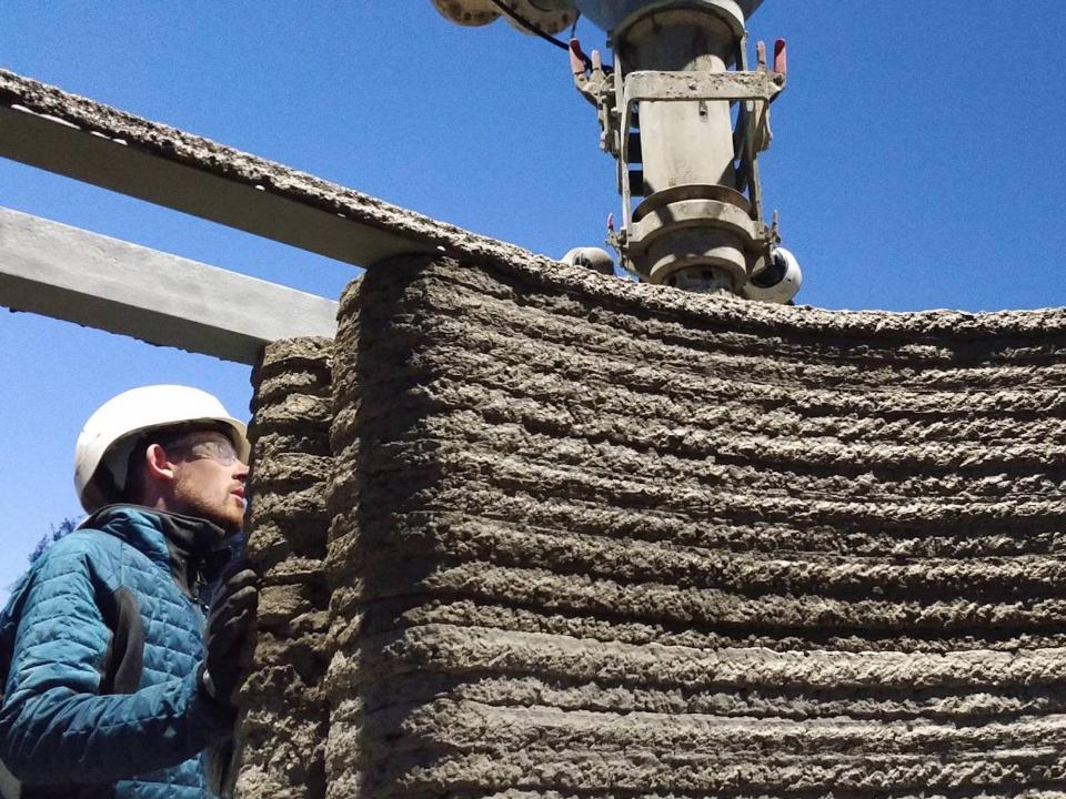 A person standing next to a 3D printed wall.