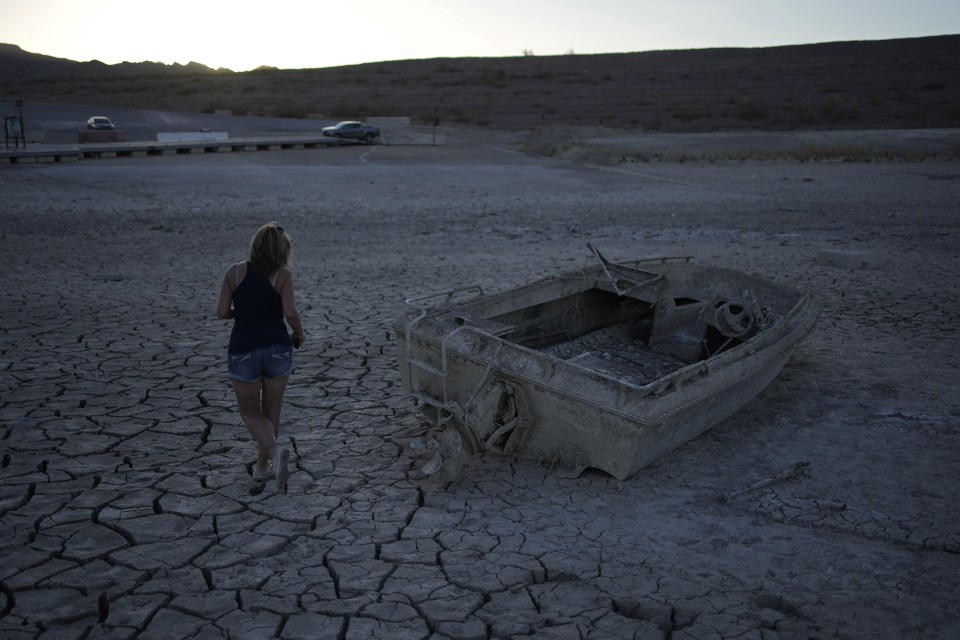 Misha McBride looks at a formerly sunken boat now on cracked earth hundreds of feet from what is now the shoreline on Lake Mead at the Lake Mead National Recreation Area, Monday, May 9, 2022, near Boulder City, Nev. (AP Photo/John Locher)