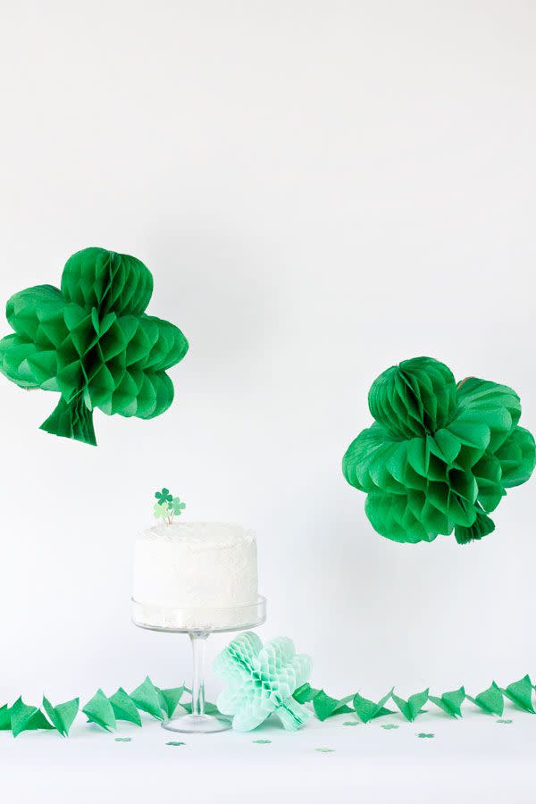 two green paper honeycomb shamrocks hanging above a white cake decorated with a green clover topper