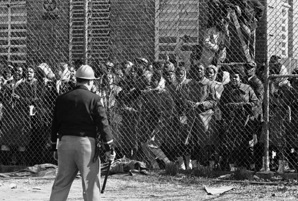 FILE - In this Feb. 4, 1965, file photo, a policeman stands guard outside a fence surrounding the Perry County Jail in Marion, Ala., as arrested civil rights demonstrators chant and sing freedom songs. As the 55th anniversary of the civil rights clash known as Bloody Sunday approaches, townspeople in Alabama want to remind the world that the road to Selma began in a place called Marion. (AP Photo/Horace Cort, File)