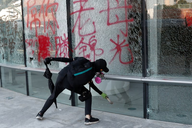 A protester breaks a glass wall sprayed with graffiti at Hong Kong Polytechnic University in Hong Kong