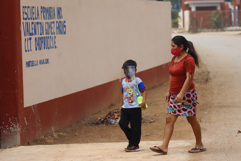 Wearing a mask to curb the spread of the new coronavirus, a mother walks her son to the first day of class at the Valentín Gomez Farias Indigenous Primary School in Montebello, Hecelchakan, Campeche state, Monday, April 19, 2021. Campeche is the first state to transition back to the classroom after a year of remote learning due to the pandemic. (AP Photo/Martin Zetina)