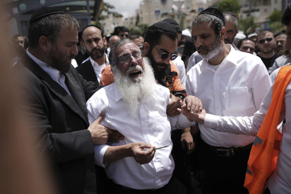 Ultra-Orthodox Jewish mourners encircle a man overcome with grief at the funeral for Yonatan Havakuk and Boaz Gol, a day after they were killed in a stabbing attack in Elad, Israel, Friday, May 6, 2022. (AP Photo/Ariel Schalit)