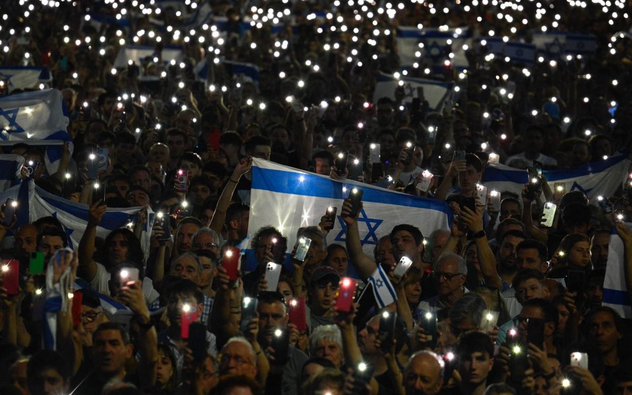 People hold Israeli national flags and display their lit mobile phones during a rally in support of the people of Israel