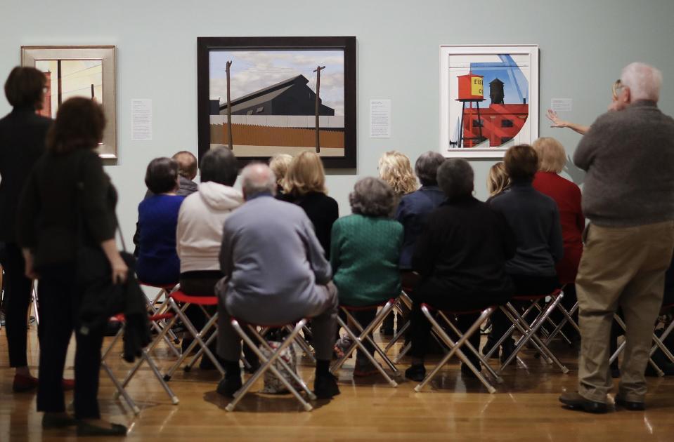 In this Monday, Feb. 6, 2017 photo, Ralston Crawford's 1936-1937 painting "Steel Foundry, Coatesville," left, and Charles Demuth's 1931 painting "Buildings Abstraction, Lancaster" are displayed as docents are given a tour of the exhibit "Cross Country: The Power of Place in American Art, 1915-1950," at the High Museum of Art in Atlanta. The new exhibition at takes a look at how American artists during the modernist period traveled outside cities to find inspiration in the rural landscape. (AP Photo/David Goldman)