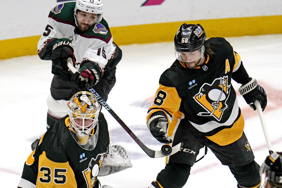 Pittsburgh Penguins' Kris Letang (58) knocks the puck off the end of the stick of Arizona Coyotes' Alexander Kerfoot (15) while defending in front of goalie Tristan Jarry (35) during the first period of an NHL hockey game in Pittsburgh, Tuesday, Dec. 12, 2023. (AP Photo/Gene J. Puskar)