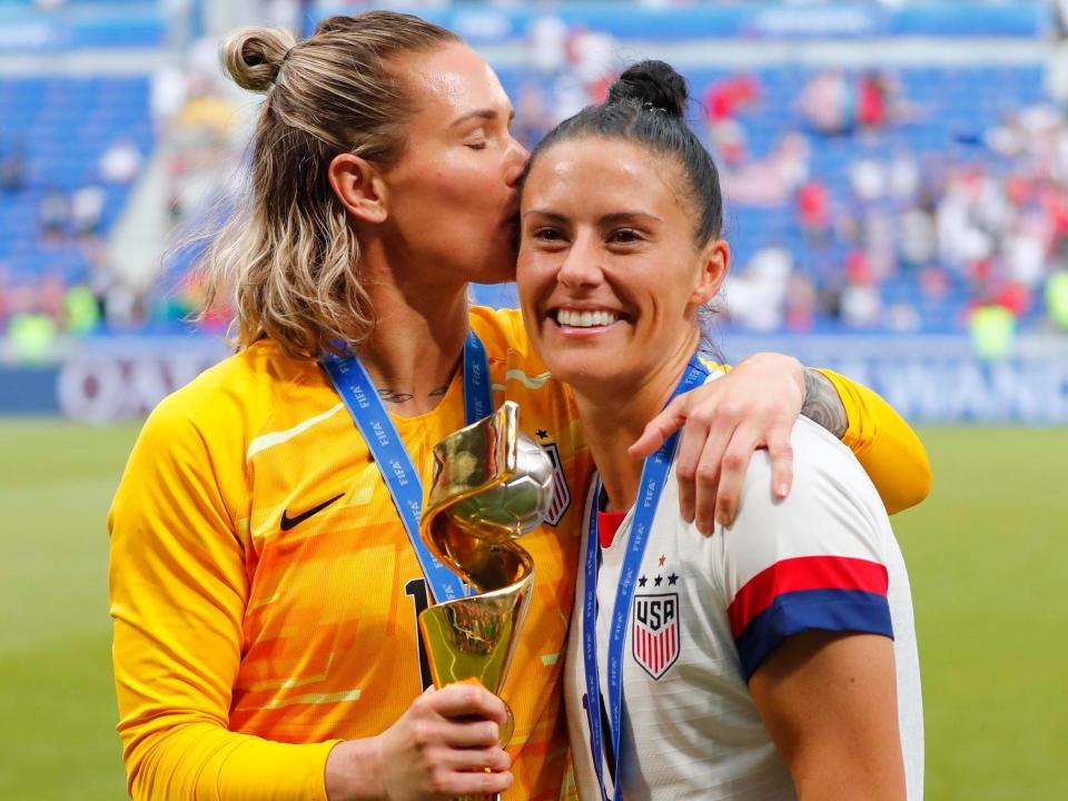 Ashlyn Harris (left) kisses Ali Krieger as they pose with the 2019 World Cup trophy.