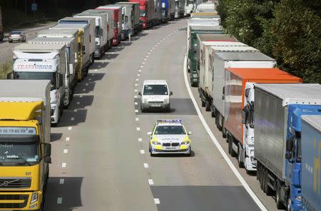 A police car passes lorries parked on the M20 motorway, which leads from London to the Channel Tunnel terminal at Ashford and the Ferry Terminal at Dover, as part of Operation Stack in southern England, Britain July 31, 2015. REUTERS/Neil Hall