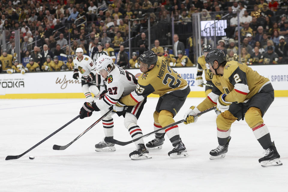 Chicago Blackhawks left wing Lukas Reichel (27) skates past Vegas Golden Knights defensemen Alec Martinez (23) and Zach Whitecloud (2) during the first period of an NHL hockey game Tuesday, April 16, 2024, in Las Vegas. (AP Photo/Ian Maule)
