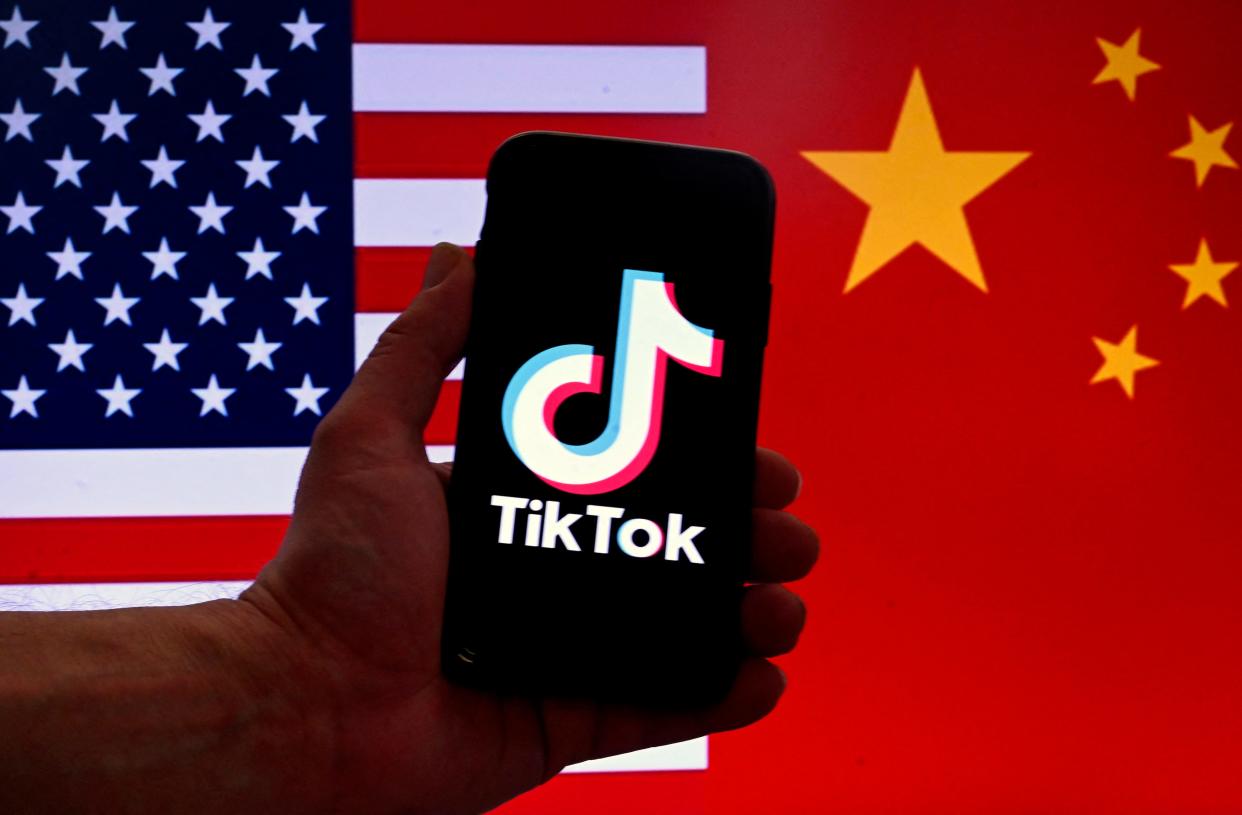 The social media application logo for TikTok is displayed on the screen of an iPhone in front of a US flag and Chinese flag background in Washington, DC.