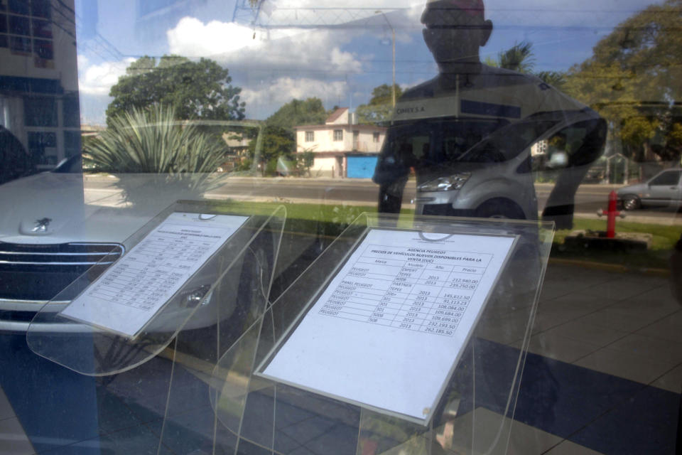 A man is reflected in the window of a car dealership as he looks at the prices of new cars, seen on the documents in the window, at a government-run dealership that sells new and used vehicles in Havana, Cuba, Thursday, Jan. 2, 2014. Cubans are eagerly visiting car dealerships as a new law takes effect on Friday eliminating a special permit requirement that has greatly restricted vehicle ownership in the country. To their dismay they found sharply hiked prices on the first day the law was in force. In Cuba, the government retains its monopoly on a vehicle's market value. (AP Photo/Ramon Espinosa)