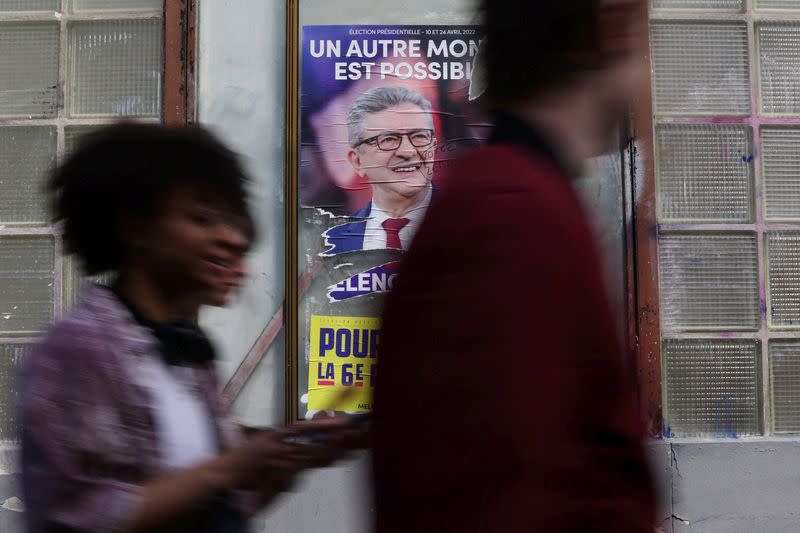 Young people walk past an official campaign poster of French far-left leader Jean-Luc Melenchon in Aubervilliers