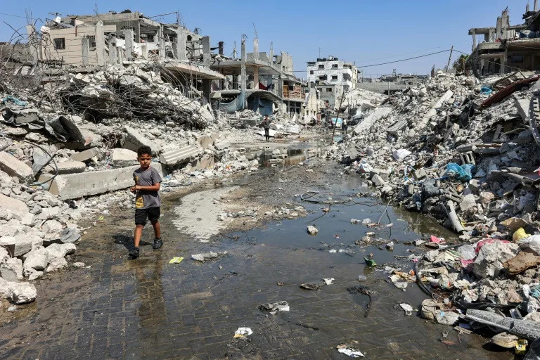 In scorching weather, a boy walks through a puddle of sewage water surrounded by mounds of garbage and rubble in Jabalia, northern Gaza -- health workers say diseases are spreading (Omar AL-QATTAA)