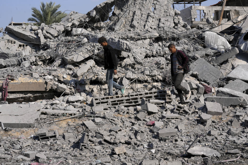 Palestinians walk by the rubble of a building of the Hamad family destroyed in an Israeli strike in Deir al Balah, Gaza Strip, Friday, Dec. 29, 2023. (AP Photo/Adel Hana)