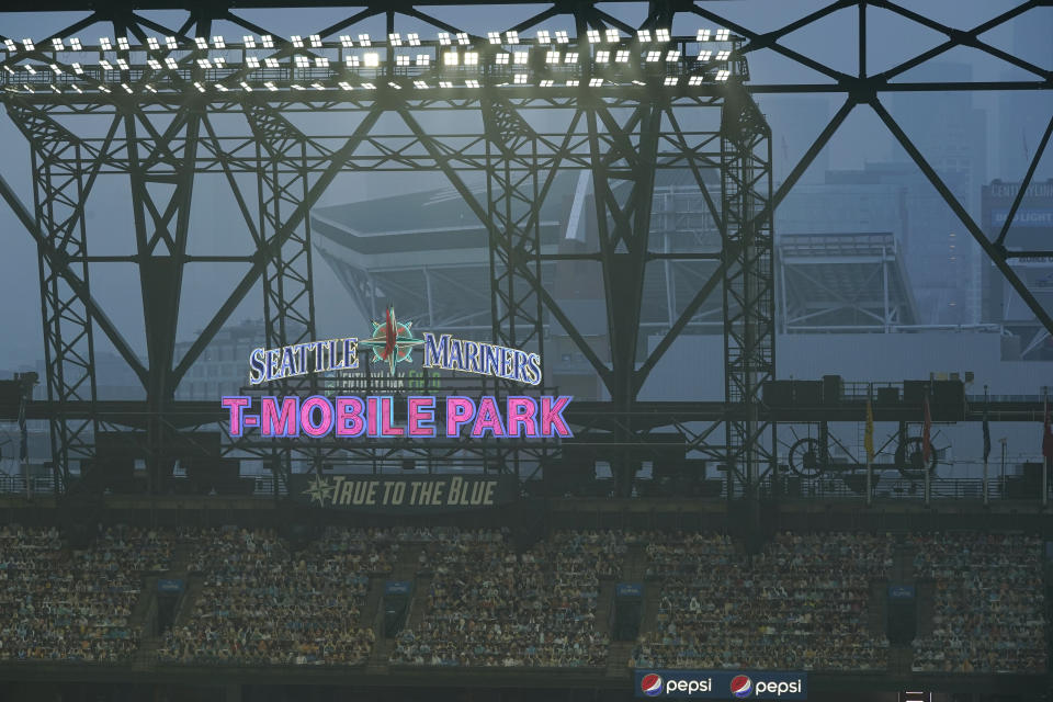 Smoke from wildfires fills the air at T-Mobile Park as photos of fans are displayed in the left field bleachers and CenturyLink Field is visible behind the ballpark sign during the second baseball game of a doubleheader between the Seattle Mariners and the Oakland Athletics, Monday, Sept. 14, 2020, in Seattle. (AP Photo/Ted S. Warren)