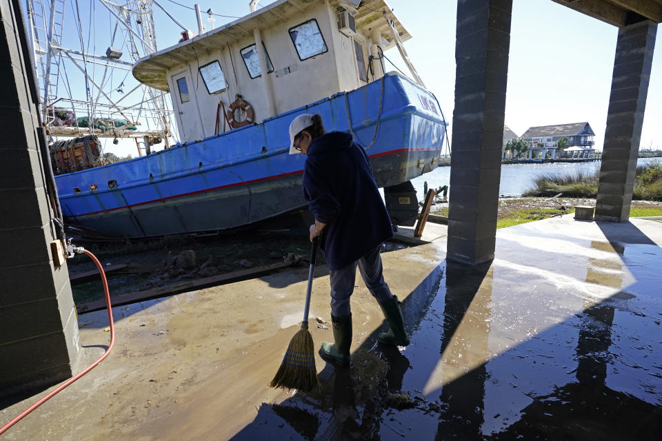 Ray Garcia sweeps water from her home after a boat washed up against it, in Lakeshore, Miss., Thursday, Oct. 29, 2020. Hurricane Zeta passed through Wednesday with a tidal surge that caused the boat to become unmoored. (AP Photo/Gerald Herbert)