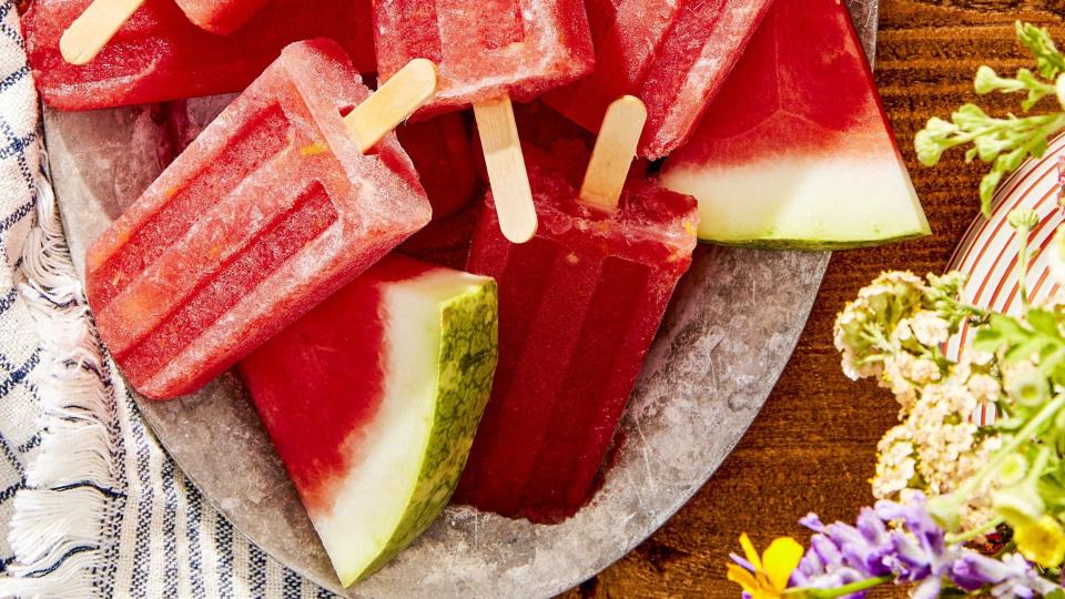 watermelon amaro pops arranged on an oval metal serving tray with slices of fresh watermelon