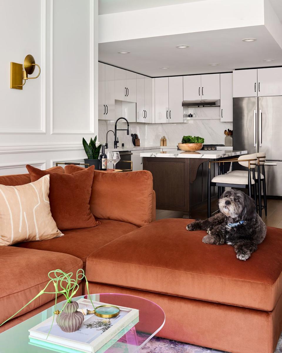 orange couch in a living room with a dog on it and the kitchen in the back