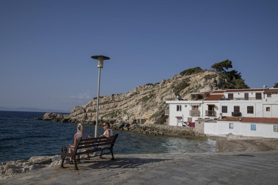 A tourist couple sit on a bench in the seaside village of Kokkari , on the eastern Aegean island of Samos, Greece, Tuesday, June 8, 2021.About a month after Greece officially opened to international visitors, the uncertainty of travel during a pandemic is still taking its toll on the country's vital tourist industry. (AP Photo/Petros Giannakouris)